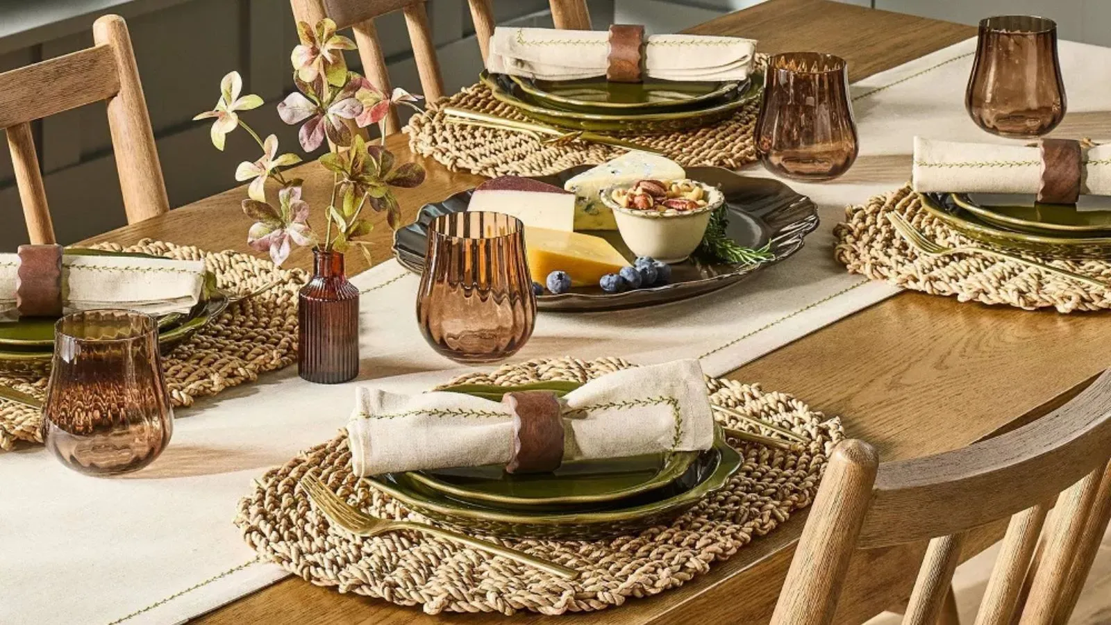 Table en bois avec sets de table en rotin, assiettes festonnées vert foncé, serviettes crème, ronds de serviette en bois et verres côtelés marron' loading='lazy' title=