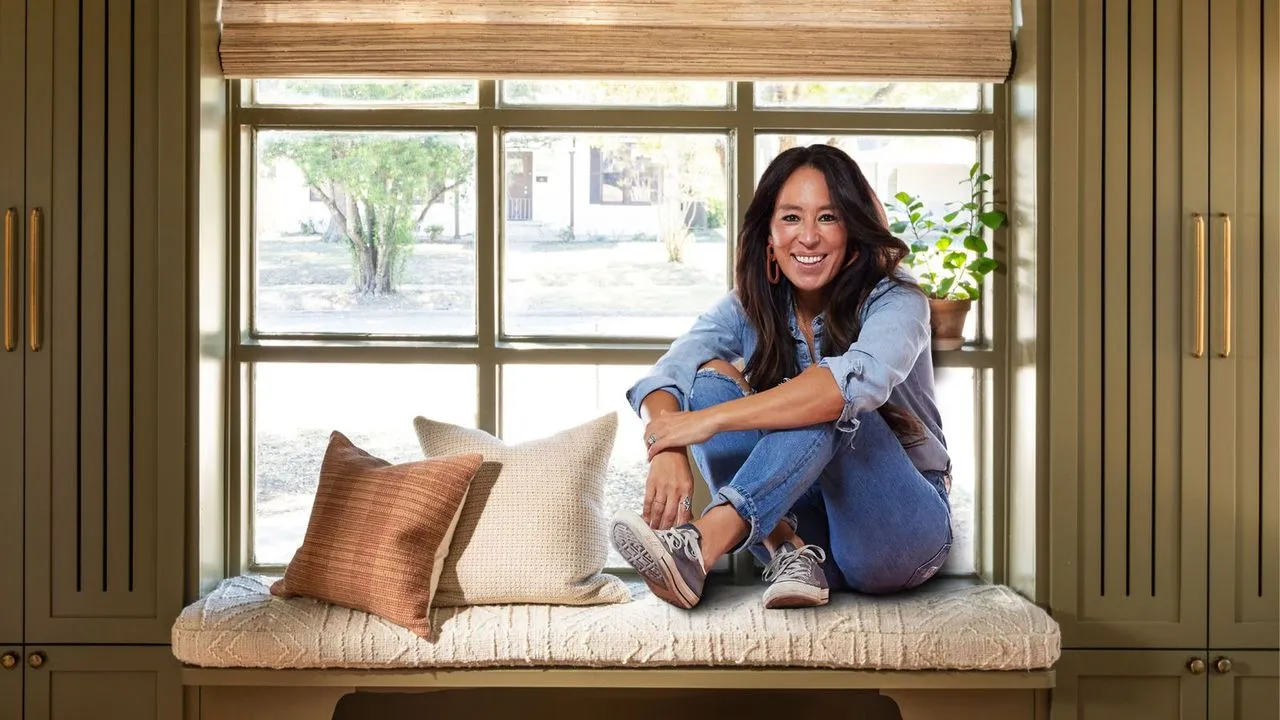 designer Joanna gaines fotografert satt på en benk i inngangspartiet med grønt skap på hver side en bambusvindusgardin og to puter' loading='lazy' title=