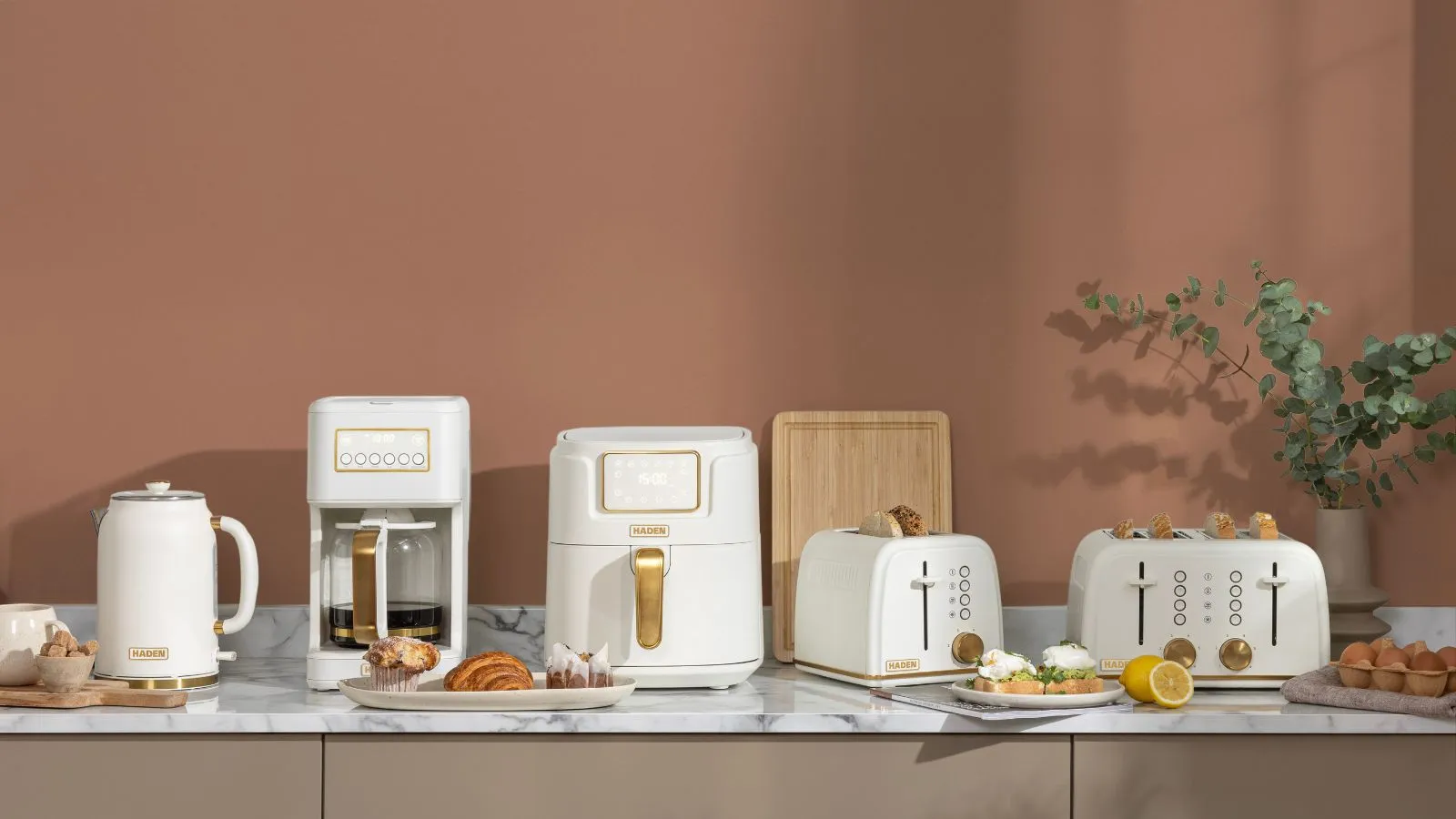 Cozinha cor de mocha com balcões de mármore branco e um conjunto de aparelhos brancos (fritadeira de ar e duas torradeiras da cafeteira e duas torradeiras) todos com detalhes em latão' loading='lazy' title=