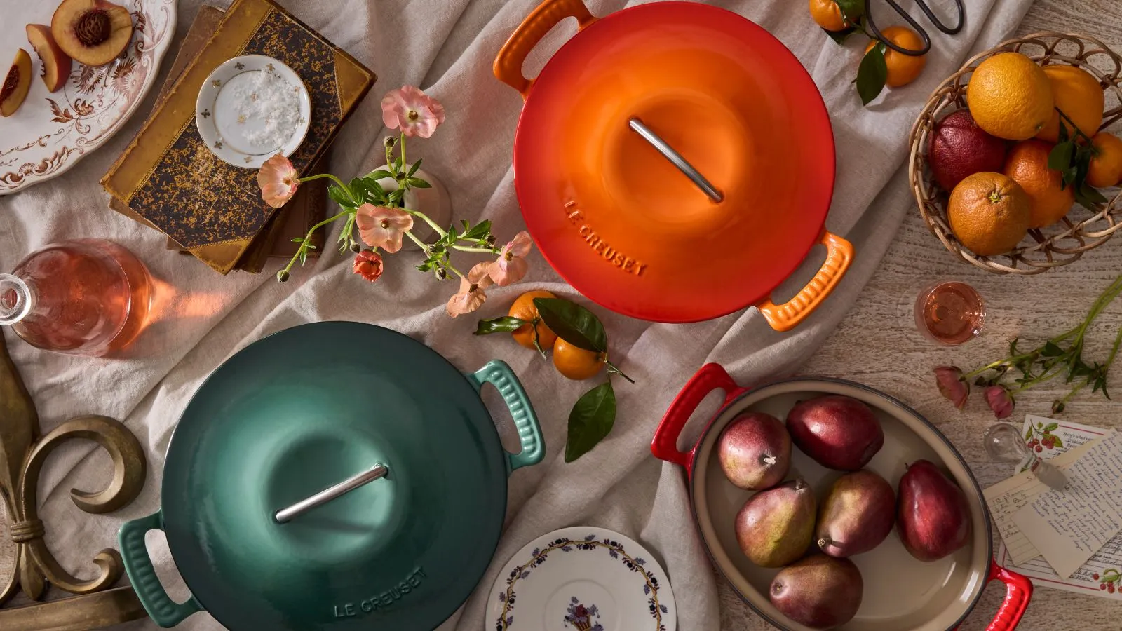 En grønn og oransje nederlandsk ovn fra den nye Le Creuset Modern Heritage Collection skutt ovenfra omgitt av frisk frukt og blomster' loading='lazy' title=