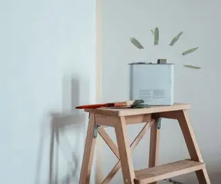 Eine Farbdose auf einer Trittleiter vor einem Malerband in einer Ecke
