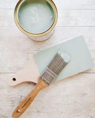 Lata de pintura con pincel y tabla de cortar parcialmente pintada con pintura verde mar.