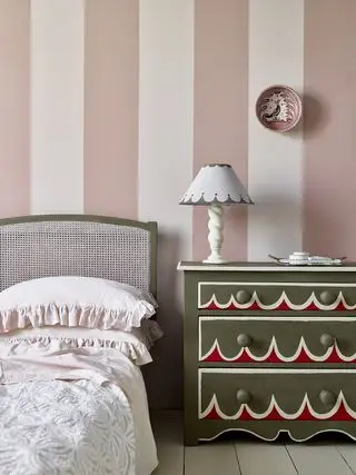 Pared pintada de rayas rosas y blancas con cabecero y cómoda de color verde salvia