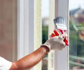Alguém usando um pincel para pintar as guarnições das janelas de branco