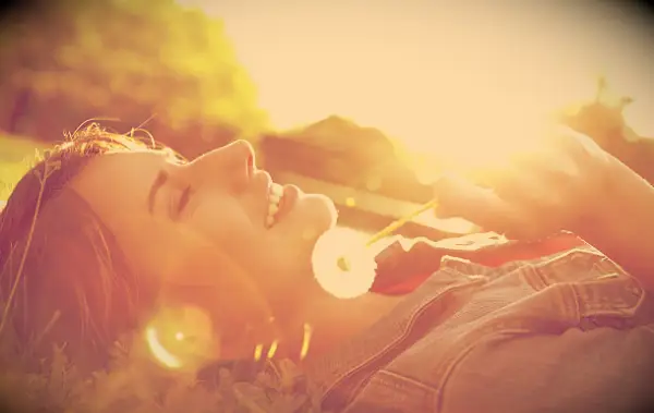 A relaxed woman lying in the grass with a dandelion in her hand.