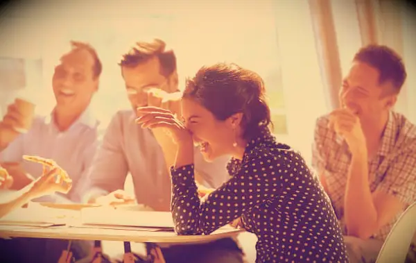 Coworkers laughing together while sitting around a table at work.