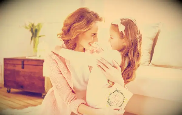 A mother embracing her smiling young daughter whole holding a Mother