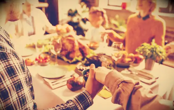 A family holding hands around a Thanksgiving dinner table.