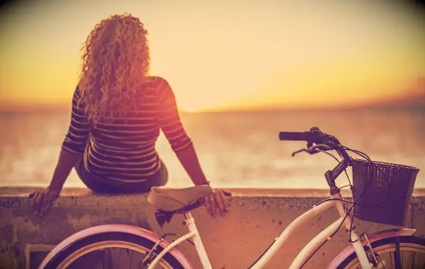 A woman sitting down to enjoy the summer sunset by the ocean.