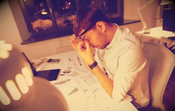 A tired looking man working late at night in an office.