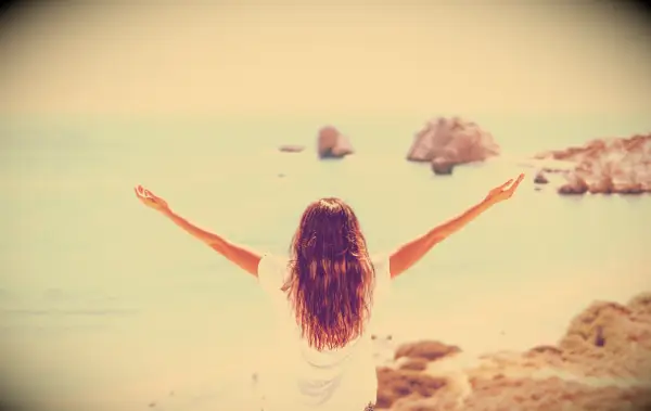 A woman raising her hand while watching the view at the ocean.