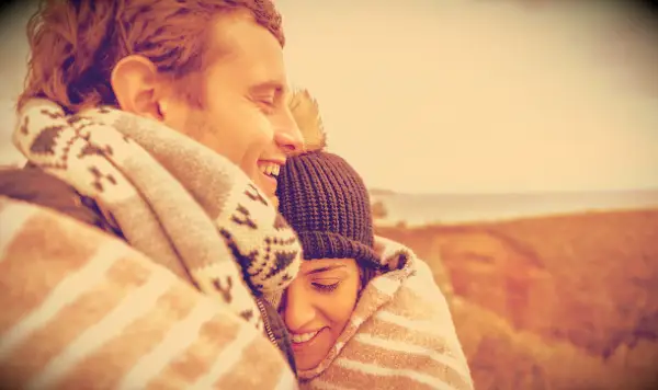 A couple hugging with blankets around them outside during fall.