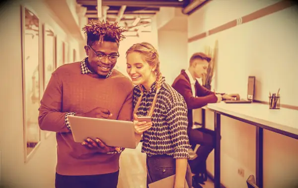 Co-workers in an office smiling while looking at a laptop screen.