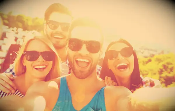 Four happy friends taking a selfie together in the summer sunshine.