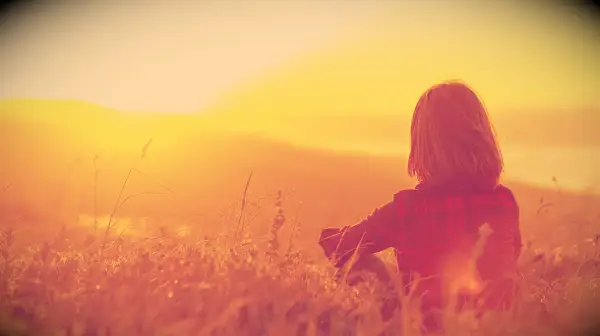 A woman sitting in a field and looking at a sunrise.