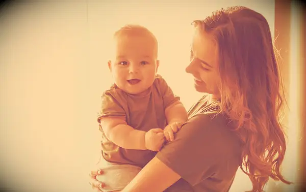 A smiling mother holding her baby who looks into the camera with a smile.