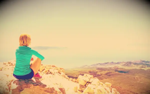 A woman on the top of a mountain looking at the vast view before her.