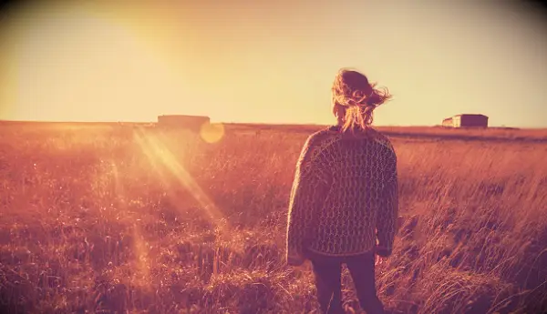 Woman looking at the sunset while standing in a late summer field.