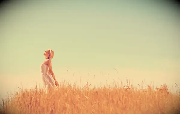 A woman stretching towards a blue sky while standing in a field.