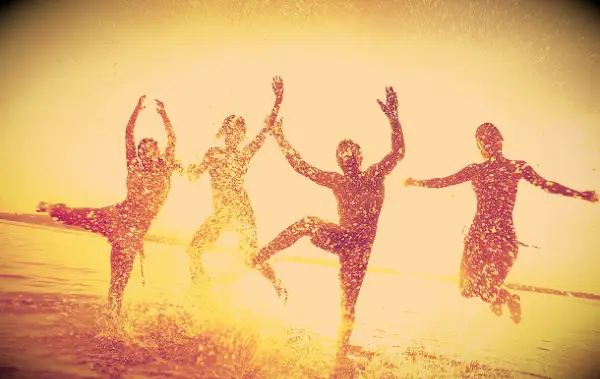 Friends having fun jumping around in the water on the beach at sunset.