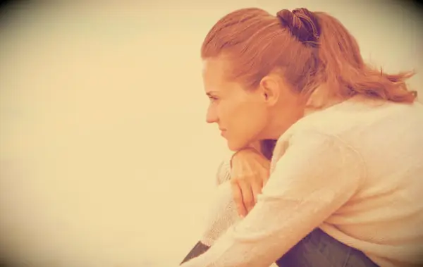 A sad woman sitting on a beach thinking.