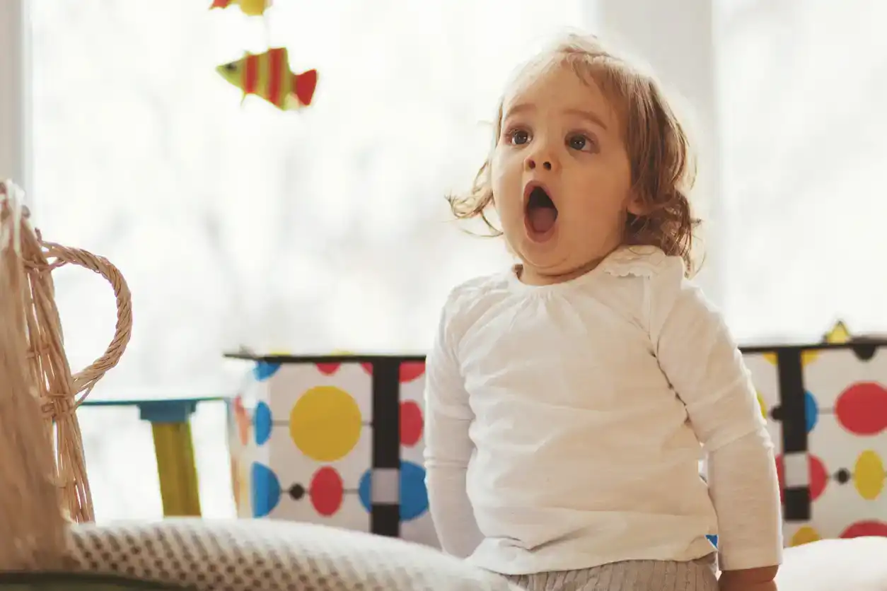 Baby girl is making funny face while playing indoors.
