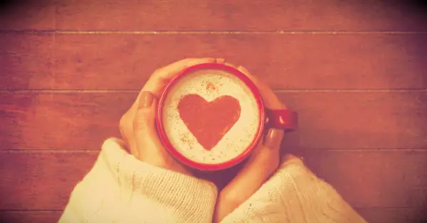 A woman holding a mug of coffee with a heartshape in the foam.