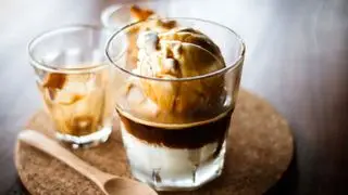 Un affogato en un vaso sobre un tablero de corcho con una cuchara de madera