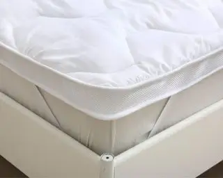 Cubrecolchón en la cama asegurado con correas y decorado con almohadas