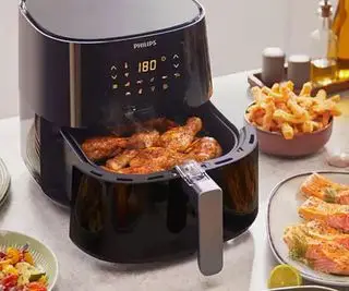 Vzduchová fritéza Philips Essentials XL na kuchynskej linke naplnená vzduchom vyprážaným jedlom.