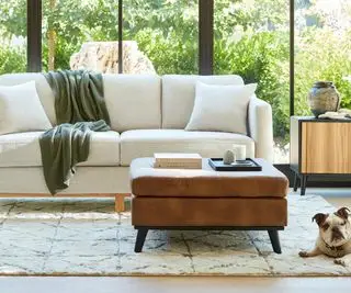 Canapé blanc avec repose-pieds contre une fenêtre avec vue sur le jardin.