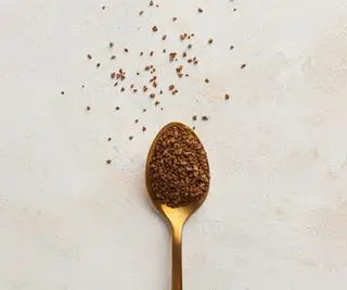Un cucchiaino d'oro con sopra del caffè solubile e un po' sparso sul piano di lavoro