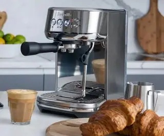 Breville Bambino Plus sobre una encimera con croissants y un café delante