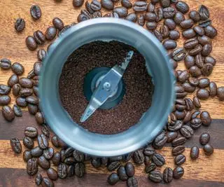 Un molinillo de hojas de café con granos de café y posos en su interior.