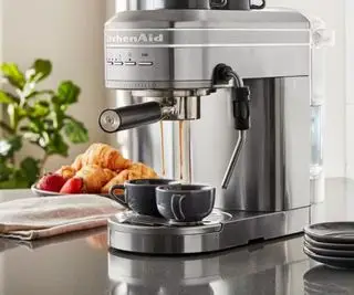 Macchina per caffè espresso KitchenAid in grigio su un piano di lavoro che prepara caffè espresso in due tazze