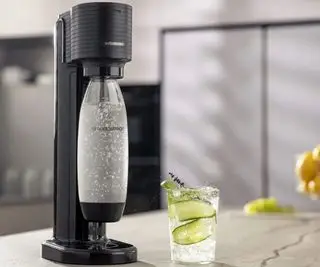 SodaStream Gaia na pracovní desce se sklenicí perlivé vody naplněné okurkou
