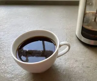 En kopp kaffe i en hvit kopp foran OXO French Press