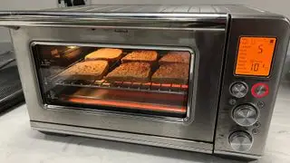 텍스트로 토스트를 만드는 스마트 오븐 에어프라이어 토스터 오븐 브레빌. 발열체에 의해 아래에서 불이 들어오고 왼쪽 화면에 기능과 시간이 나열된 주황색 불이 들어옵니다.