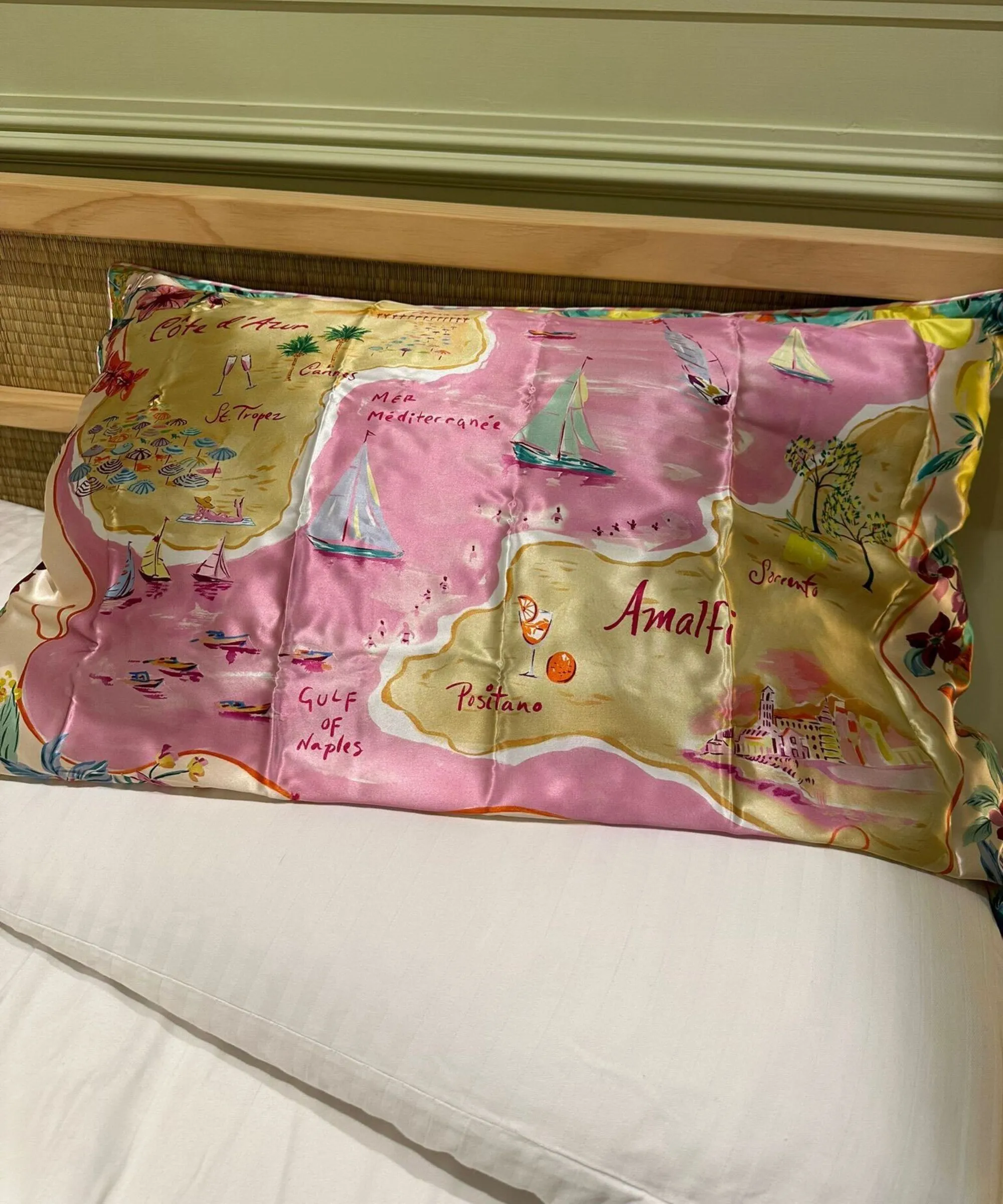 Pink mønstret Slip silke pudebetræk på hvidt sengetøj med en rattan Japandi sengegavl og grøn væg med panel bagved.' loading='lazy' title=