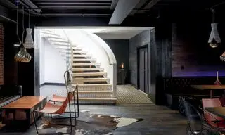 Escalier hélicoïdal menant au sous-sol avec murs en bois sombre et briques, coin salon et table à manger