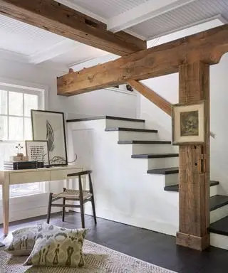 Sous-sol d'une propriété d'époque avec poutres et colonnes en bois apparentes, lambris en bois blanc, escalier blanc et en bois menant au sous-sol, bureau en bois donnant sur la fenêtre