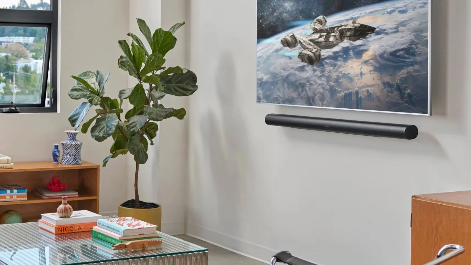Sonos Arc Ultra pod telewizorem wyświetlającym scenę kosmiczną w białym salonie ze stolikiem kawowym ze szkła roślinnego, drewnianą półką na książki i częściowo otwartym oknem.' loading='lazy' title=
