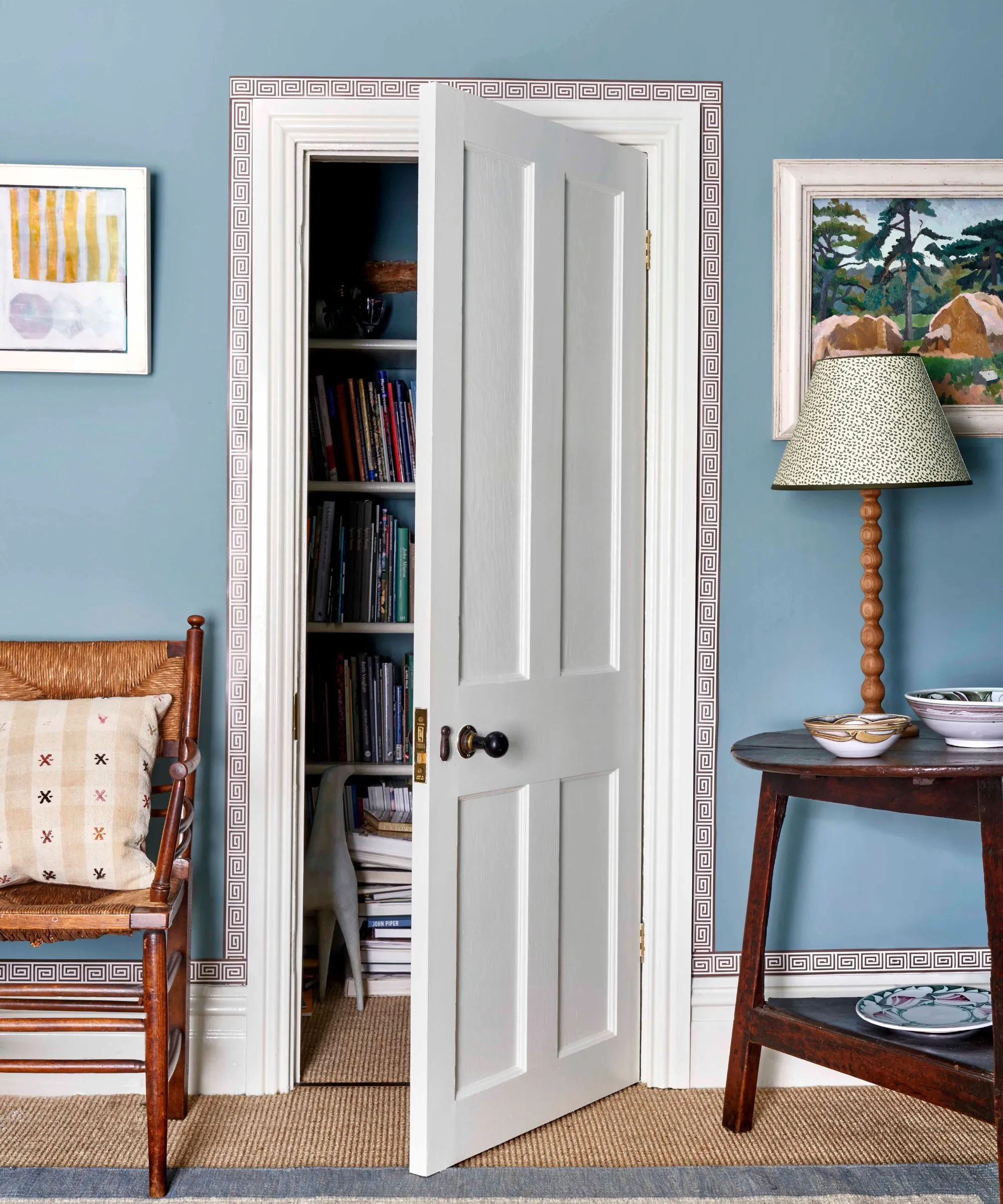 Una porta bianca parzialmente socchiusa che mostra un ripostiglio. Parete dipinta di blu con un piccolo bordo rosso e bianco attorno al telaio della porta.' loading='lazy' title=