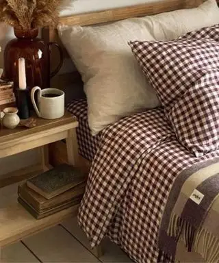Literie en vichy aux baies sur un lit à côté d'une table de nuit remplie de pendentifs et de livres