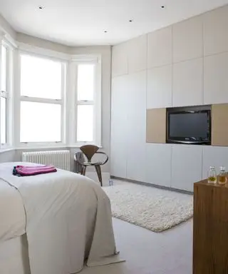 Uma ideia de TV no quarto com cama branca e decoração de parede, com TV instalada como parte do guarda-roupa branco