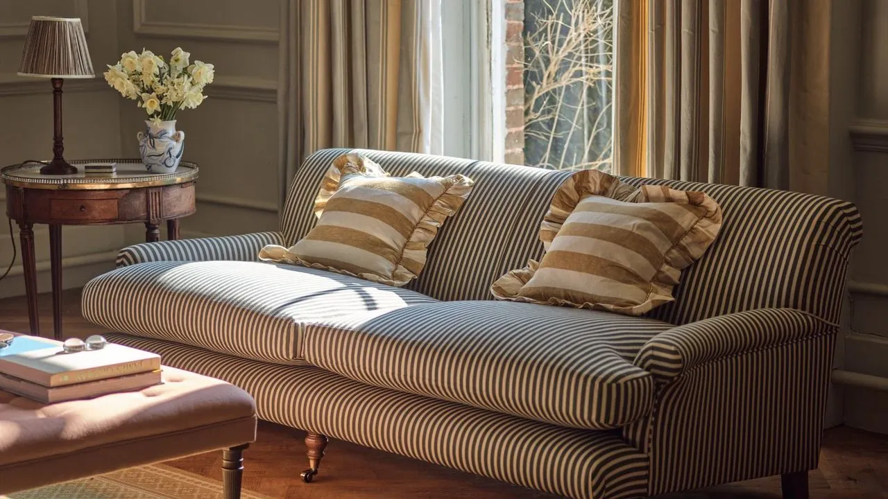 En svart og hvit pinstripe sofa i en tradisjonell stue. Et lite sidebord i tre med en lampe og en vase med blomster ved siden av. Hvite og gulstripete puter på den.' loading='lazy' title=