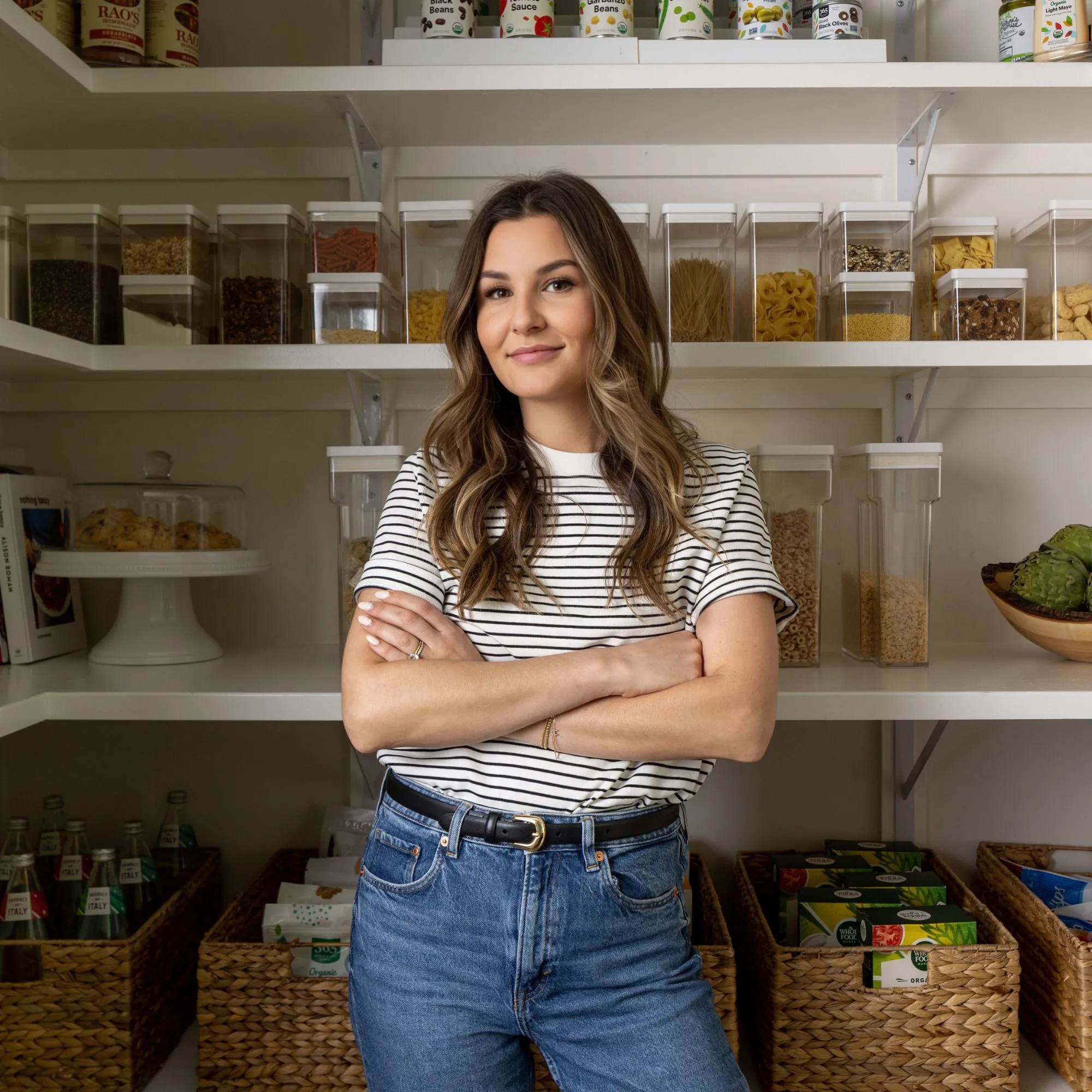 티셔츠와 청바지를 입고 식료품 저장실에 서 있는 Ashley La Fond의 사진과 뒤에 캔이 놓여 있습니다.' loading='lazy' title=