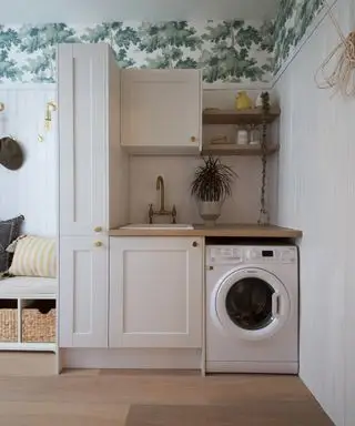 Lámpara de pared Industville Sleek Edison - Imagen de latón: un cuarto de lavado neutro con papel tapiz verde y blanco y un banco en la entrada a la izquierda