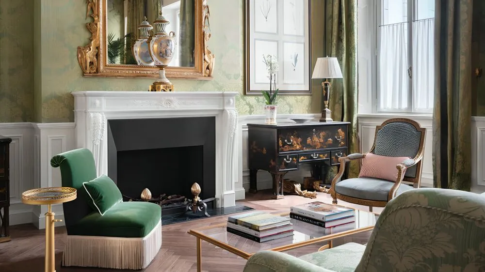 Ein traditionelles Wohnzimmer mit grüner Tapete, einem großen Kamin, einem Couchtisch aus Glas und grünen Sesseln.' loading='lazy' title=