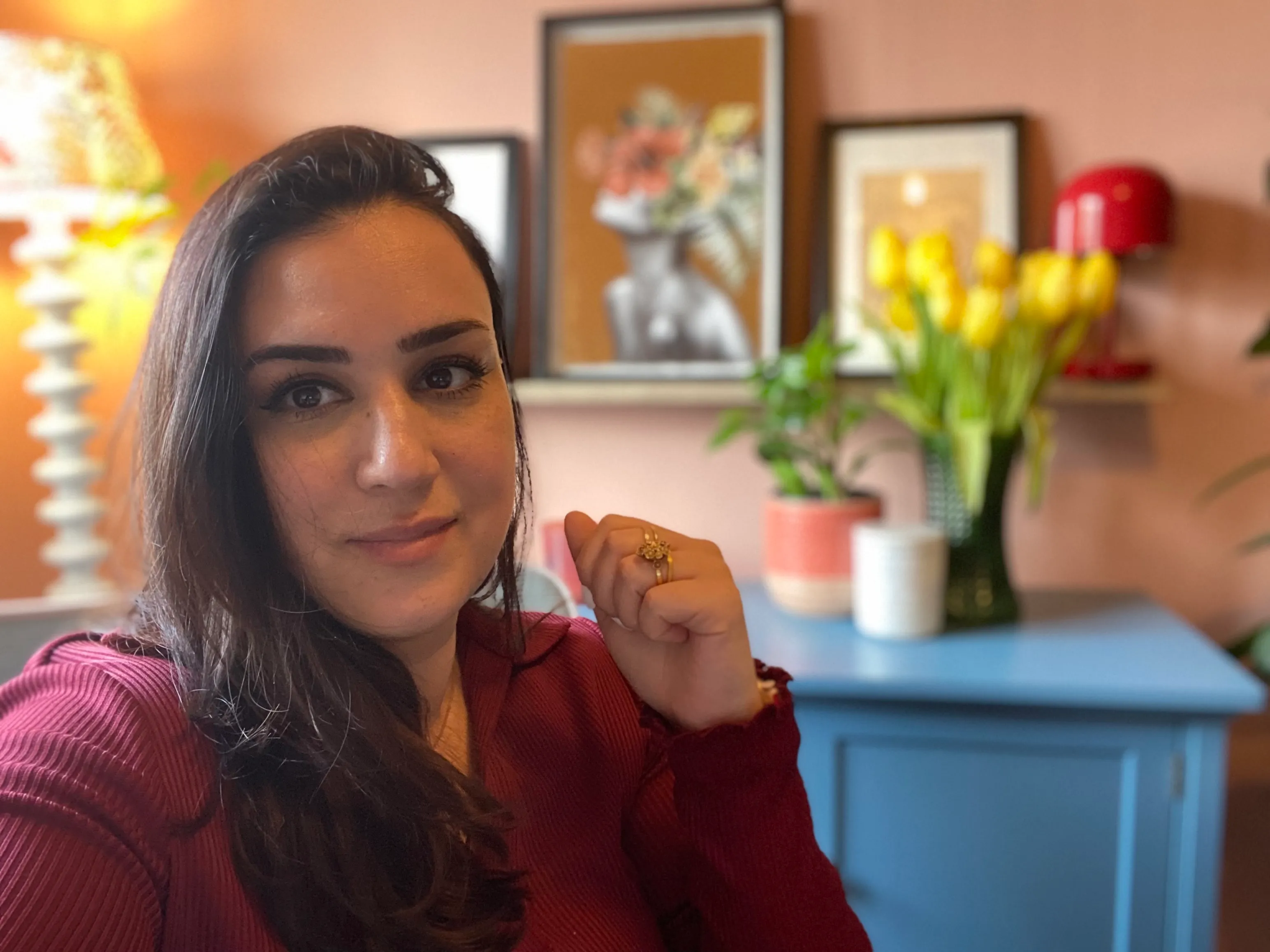 Foto da cabeça da morena Punteha em um vestido de manga comprida com gola cor de vinho contra um fundo de parede pintado de terracota' loading='lazy' title=